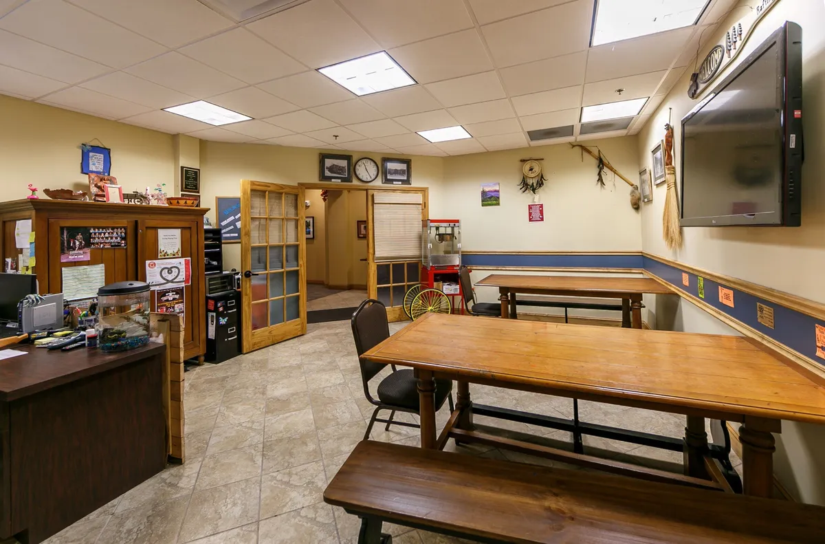 The image captures the resort's cozy and communal interior space, with wooden tables, a reception desk, and a relaxed gathering area. The mood is warm and inviting, suggesting a space where families can regroup and socialize after a day of exploration.