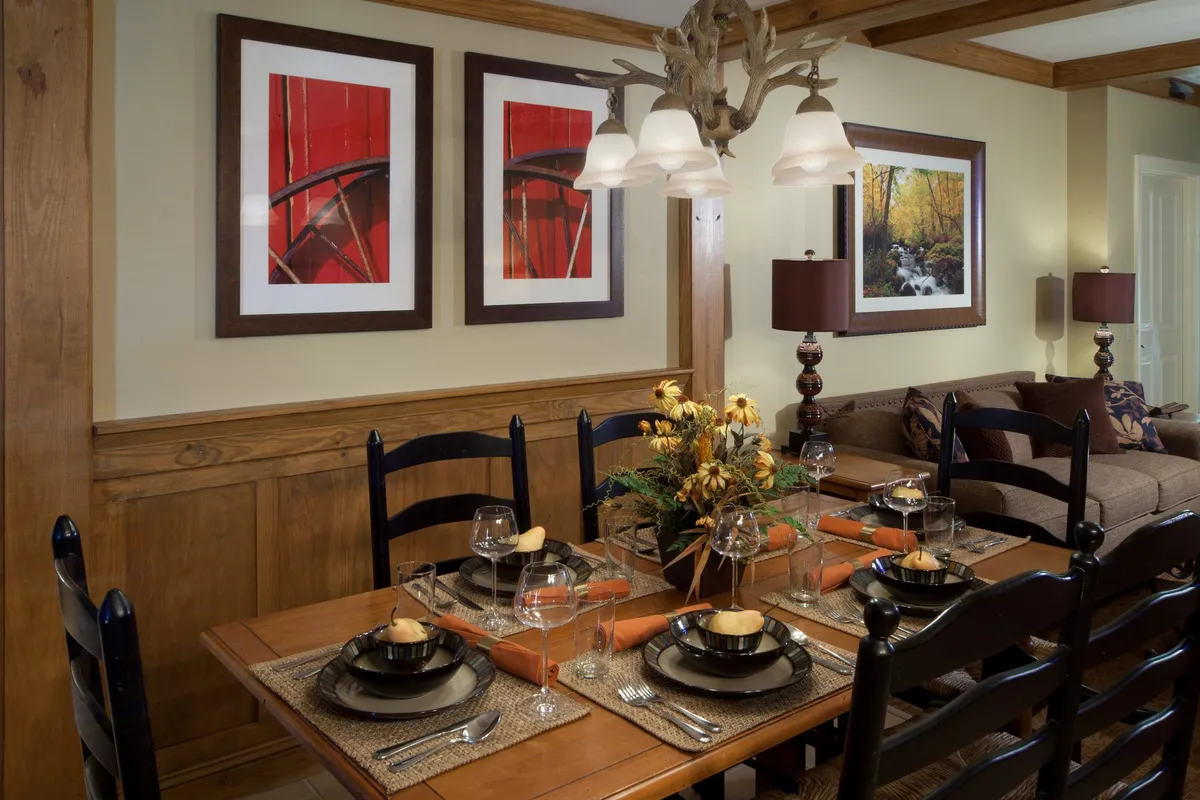 This image displays a well-appointed dining area featuring a wooden table, elegant chandelier, floral centerpiece, and tasteful wall art. The inviting atmosphere is perfect for family dinners, celebrations, or intimate gatherings.