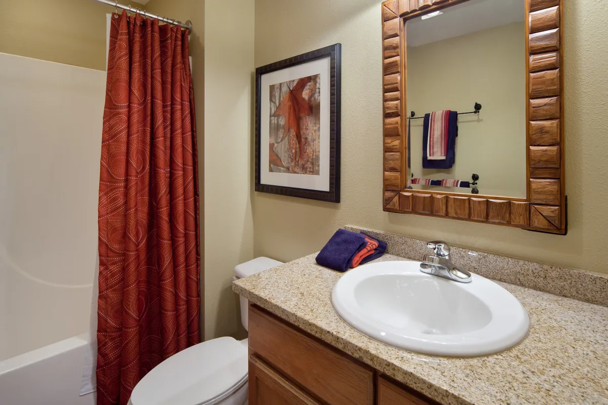 A comfortable bathroom with a soft glow, showing a modern sink, large mirror, and a shower with a curtain. The tranquil mood suggests a space for self-care and quiet solitude.