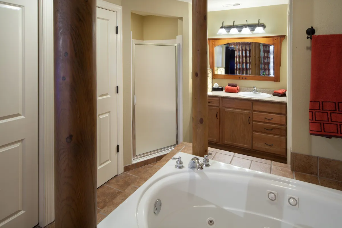 A spa-inspired bathroom featuring a luxurious jacuzzi tub framed by elegant wooden columns, a well-lit vanity mirror, and high-end bathroom fixtures. The tranquil ambiance suggests a space designed for self-care routines and relaxation after a busy day.