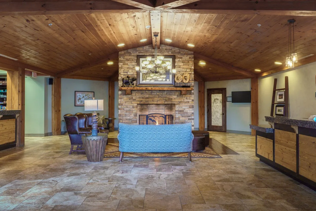 This image captures a warmly lit living area featuring a blue sofa set beside a rustic stone fireplace, with exposed wooden beams overhead. The space suggests both comfort and character, encouraging relaxation and making guests feel at home.